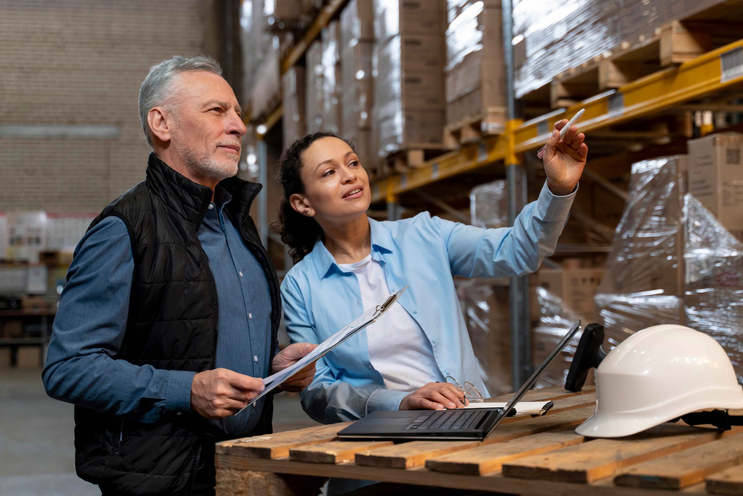 A male and female in a large warehouse looking up at boxes stacked on shelves. They are smiling.